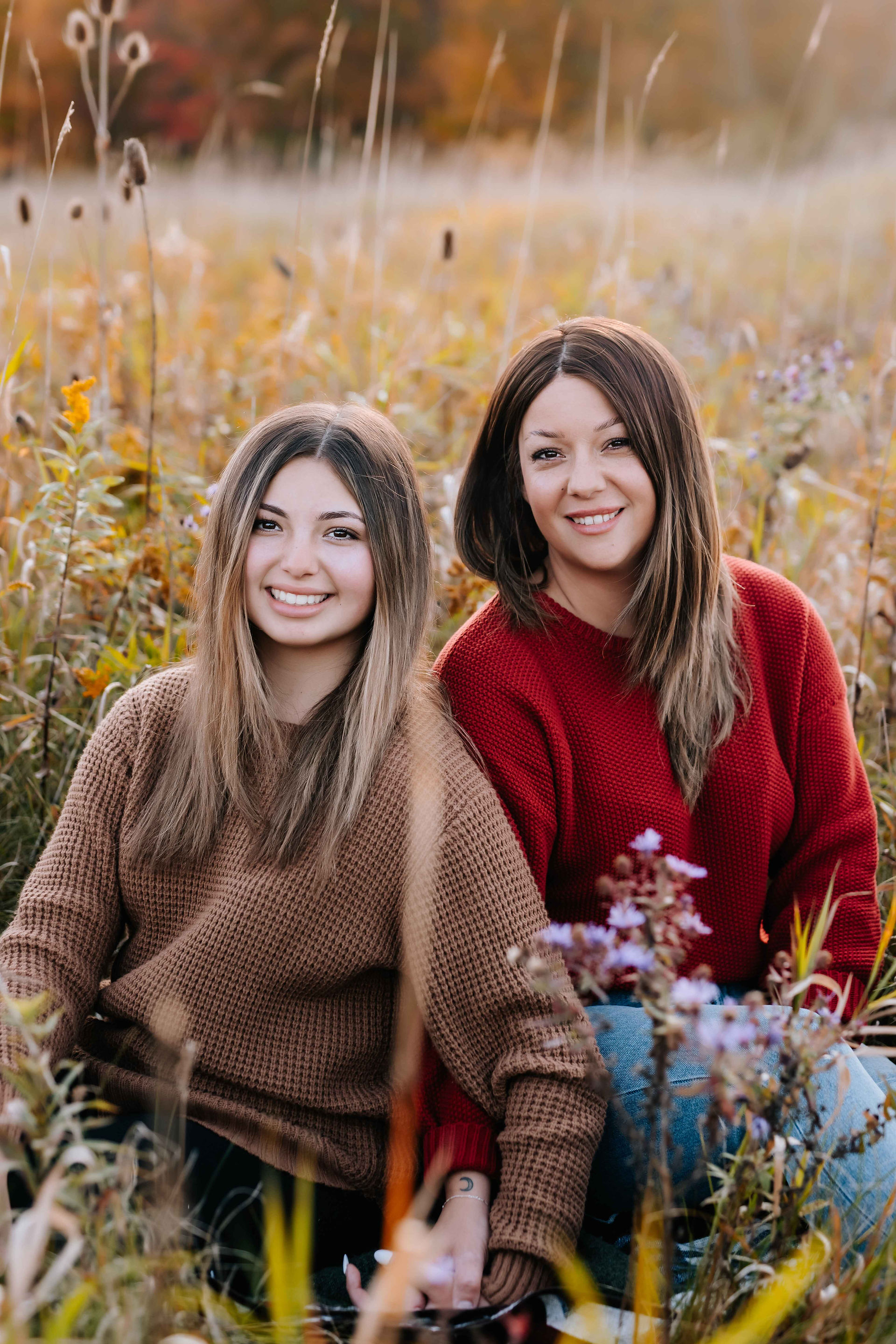 A mother and daughter sitting in tall grass during the fall in Niagara smiling t the camera.