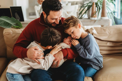 A dad and his sons sitting in their living room embracing the new baby.