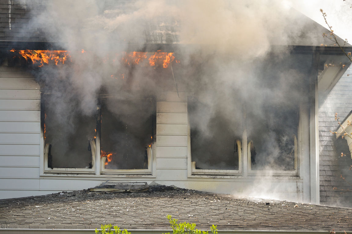 Smoke billows from a house fire with windows broken and charring on the roof