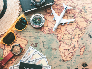 Travel flat lay on a world map: camera, toy airplane, compass, sunglasses, watch, hat, cash, and plant; Indian Ocean visible.