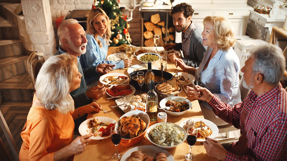 Multi-generational family shares a festive holiday dinner at a long table, smiling near a lit Christmas tree and wine glasses.