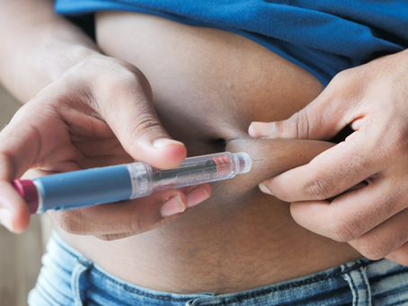 Close-up of hands injecting insulin into a bare abdomen, with a blue shirt and jeans visible, suggesting careful self-care