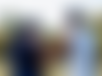 Man in white shirt with his arm around a woman in a blue shirt, walking in a sunny park with trees. Mood is supportive and caring.