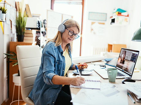 Mature woman working from home on laptop. Woman has blueprints on the table, dealing with investments and finances.
