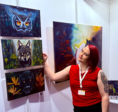 Artist pointing at various animal paintings, owl, wolf, panther, AC Brune FineArt Web.