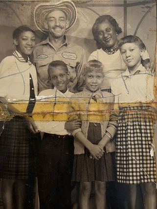 Vintage photo of a smiling family. Two adults, four children; the man wears a hat. Background is simple. The image is aged and worn.