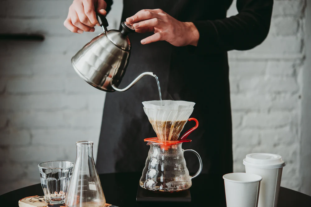 Barista pouring hot water from a gooseneck kettle over Witch Coffee Black Label coffee grounds