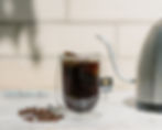 A transparent glass of Witch Coffee Black Label single-serve coffee bag, on a table with 100% Arabica coffee beans.