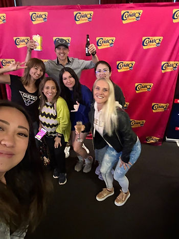 A group of friends posing in front of The Comics Lounge banner
