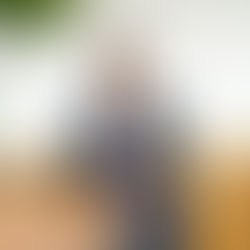 Eine lächelnde Person mit Headset hält ein Tablet auf einem beigen Ledersofa. Der Hintergrund ist neutral, ein Glas Wasser steht daneben.