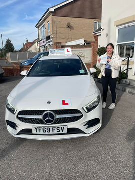 Proud learner with test certificate standing beside car