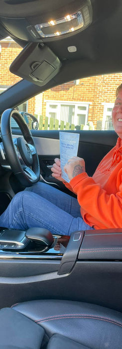 Student holding pass sheet beside white driving school car