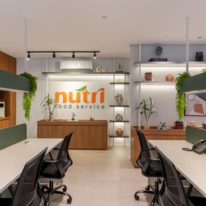 Escritório comercial Nutri Food Service com bancadas de trabalho, cadeiras de escritório, logo ao fundo. Detalhes em laranja e verde
