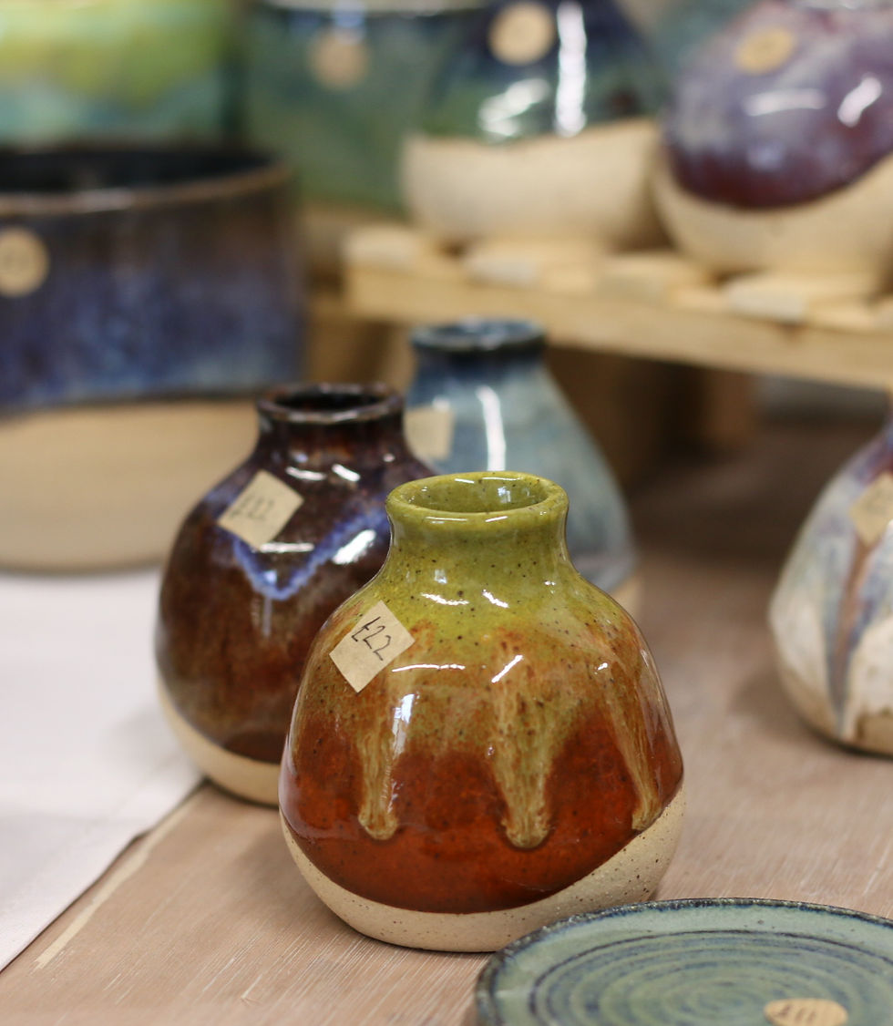 Colorful ceramic vases with numbered tags sit on a wooden table. The vases have green, red, and brown hues with a glossy finish.
