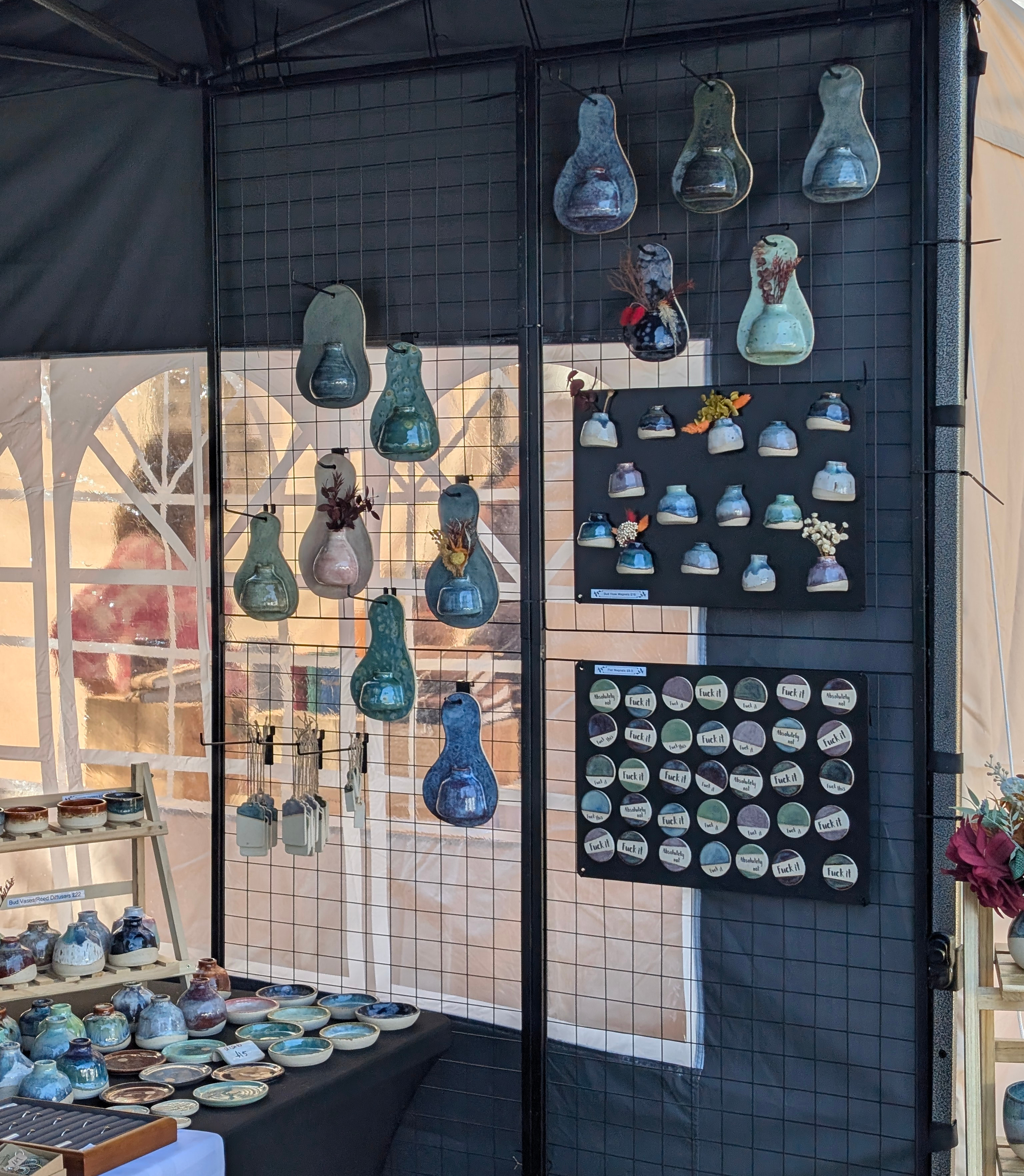Handmade colourful ceramic wall hangings and magnets on a grid wall attached to a black gazebo