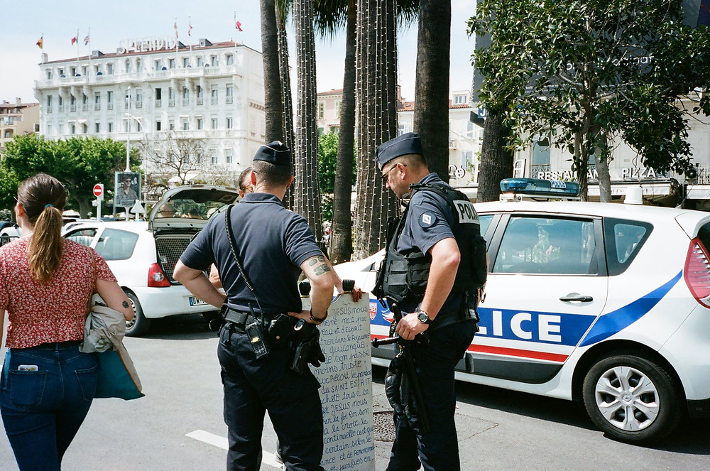 two police men standing near another person beside white and blue police vehicle on road