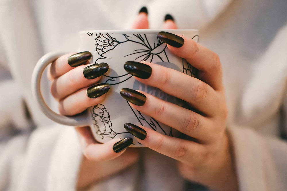 close up photography of a woman in black nail polish holding a mug