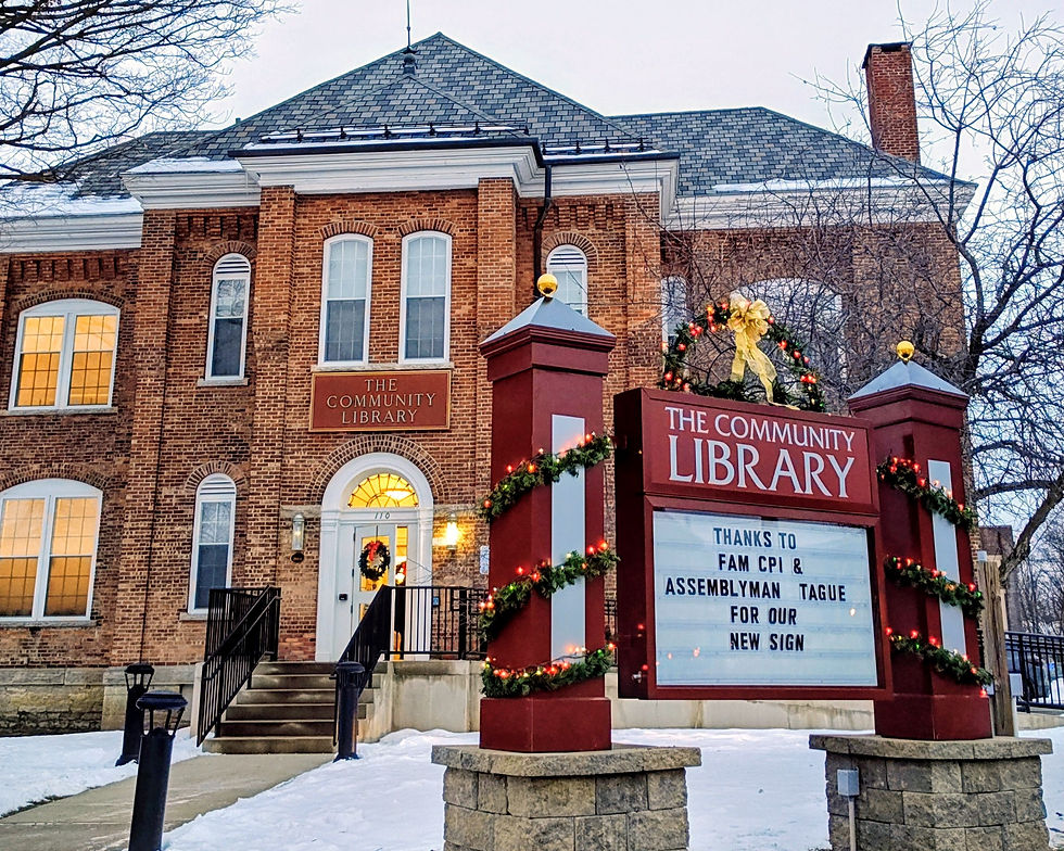 The Community Library in winter, showing the brick building and a newly installed exterior sign decorated with holiday greenery.