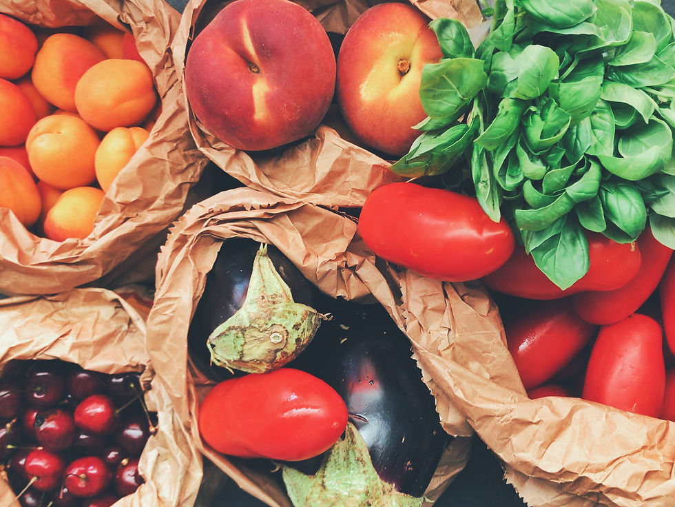 Apricots, peaches, basil, tomatoes, eggplant, and cherries are shown in brown paper shopping bags.