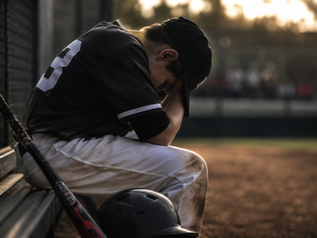 A young baseball player sitting along on a dugout bench after a difficult moment in a game, representing pressure, confidence, and resilience in youth sports.