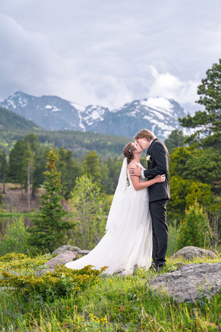 a bride and groom kissing with mountains in the background