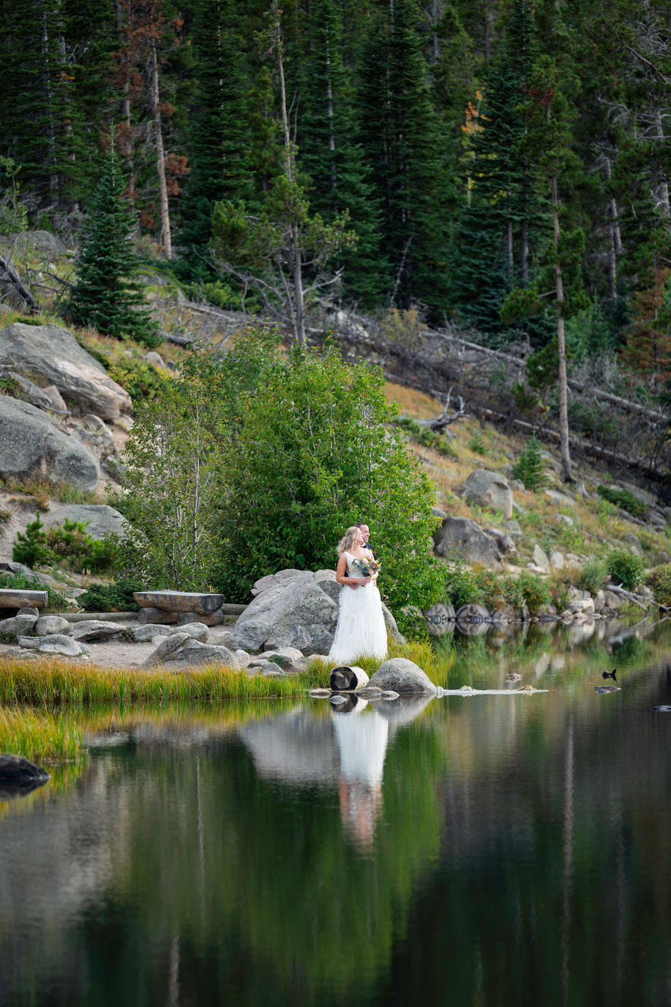 Bride standing by a serene lakeside landscape.