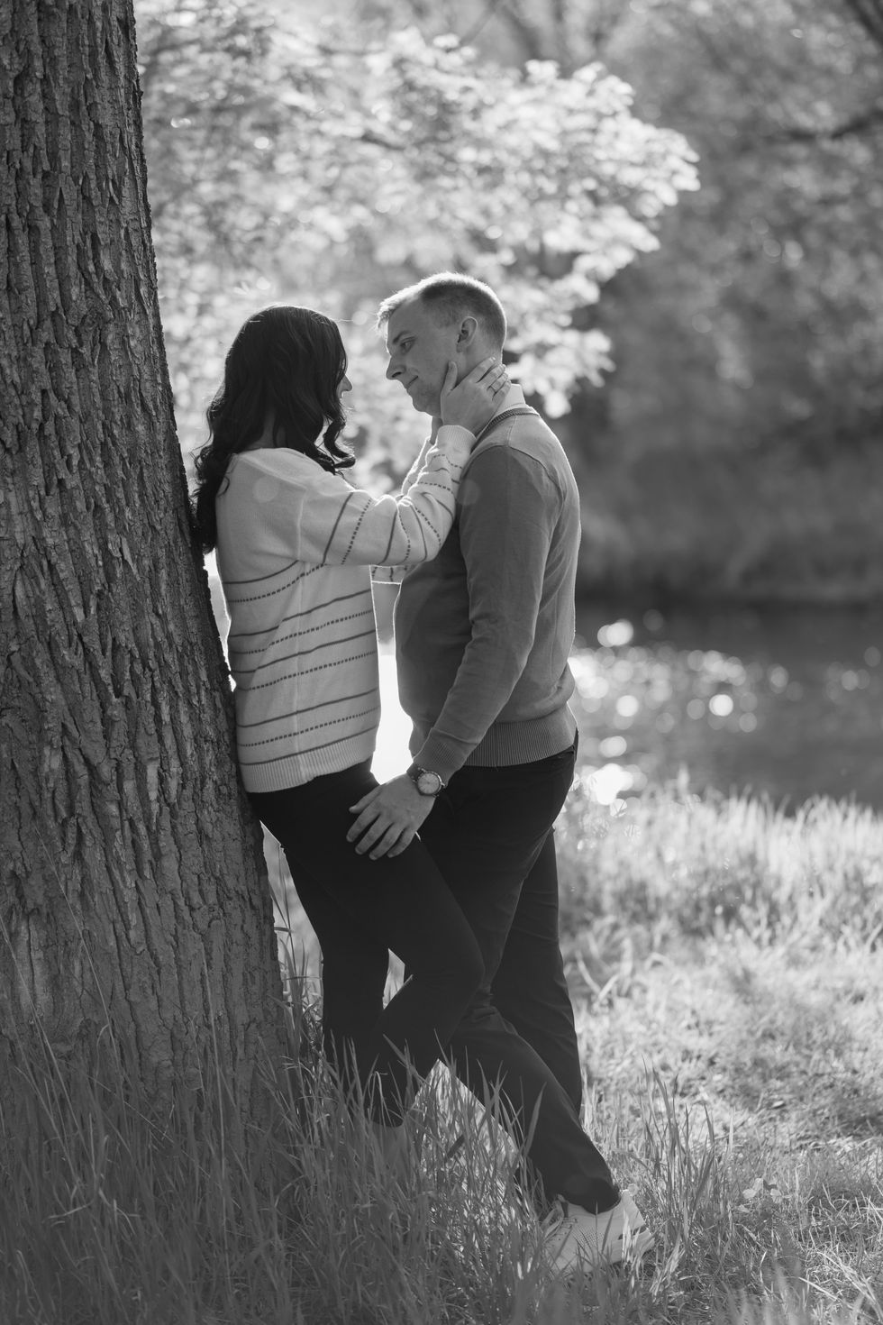 a black and white photo of a man and woman leaning against a tree