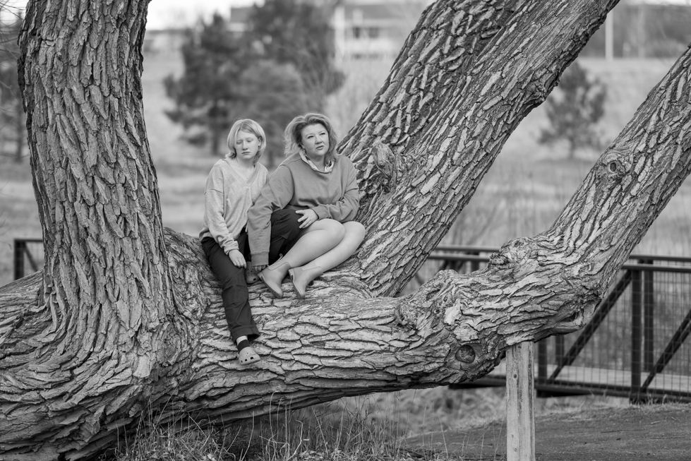 two women sit on a tree branch in a black and white photo
