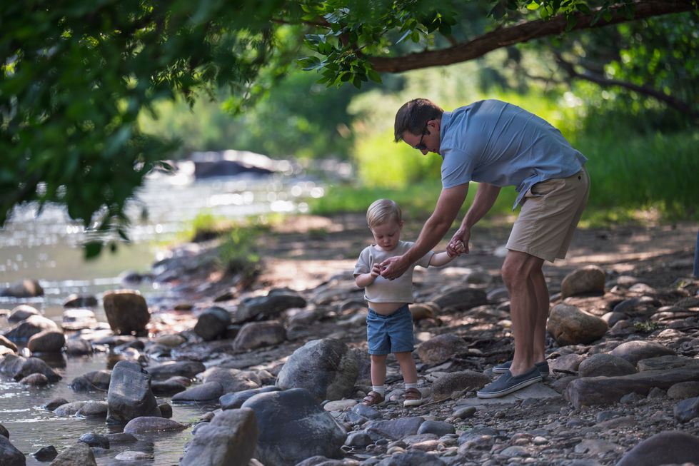 Adult helping child on rocky riverbank path.