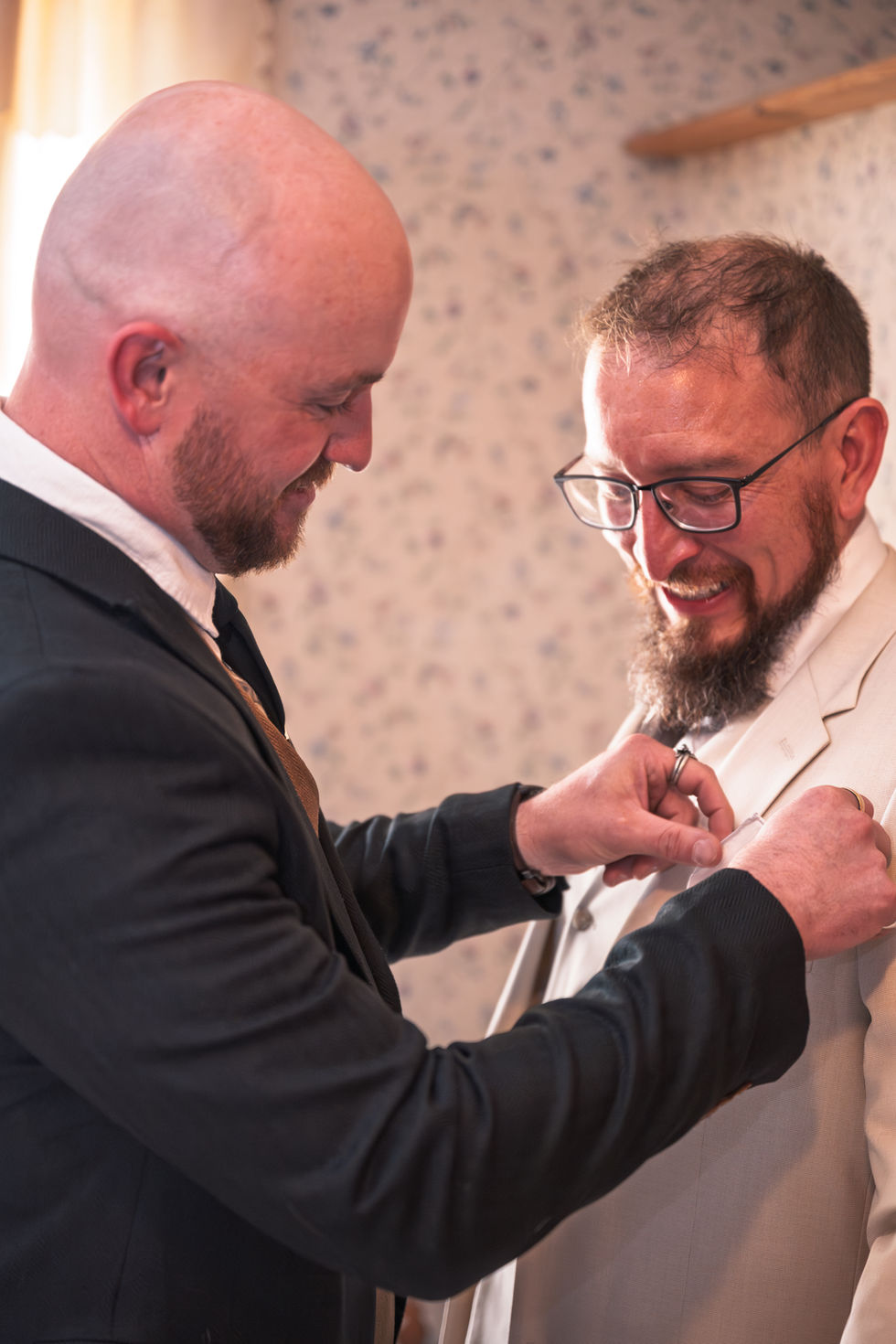 Two men adjusting a suit and tie indoors.