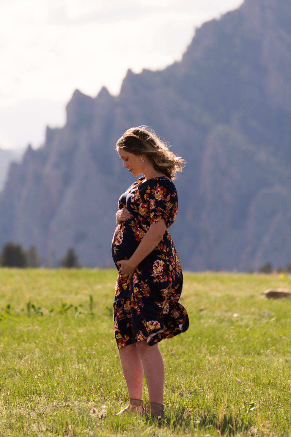 a pregnant woman in a floral dress holds her belly in a field