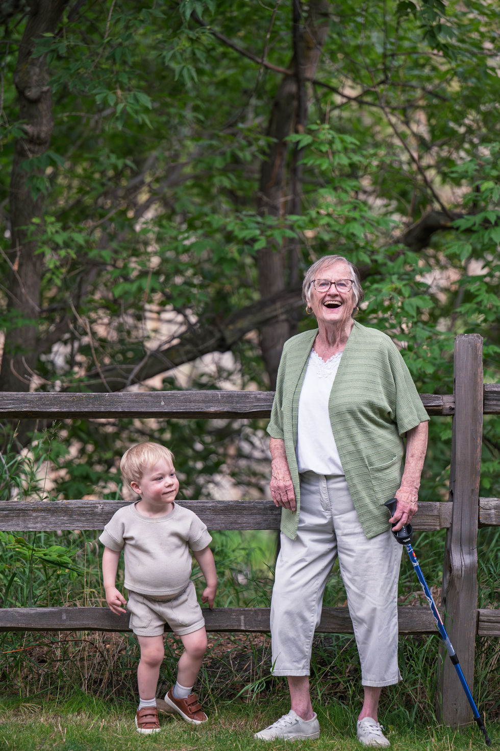Elderly woman and child smiling by a wooden fence.