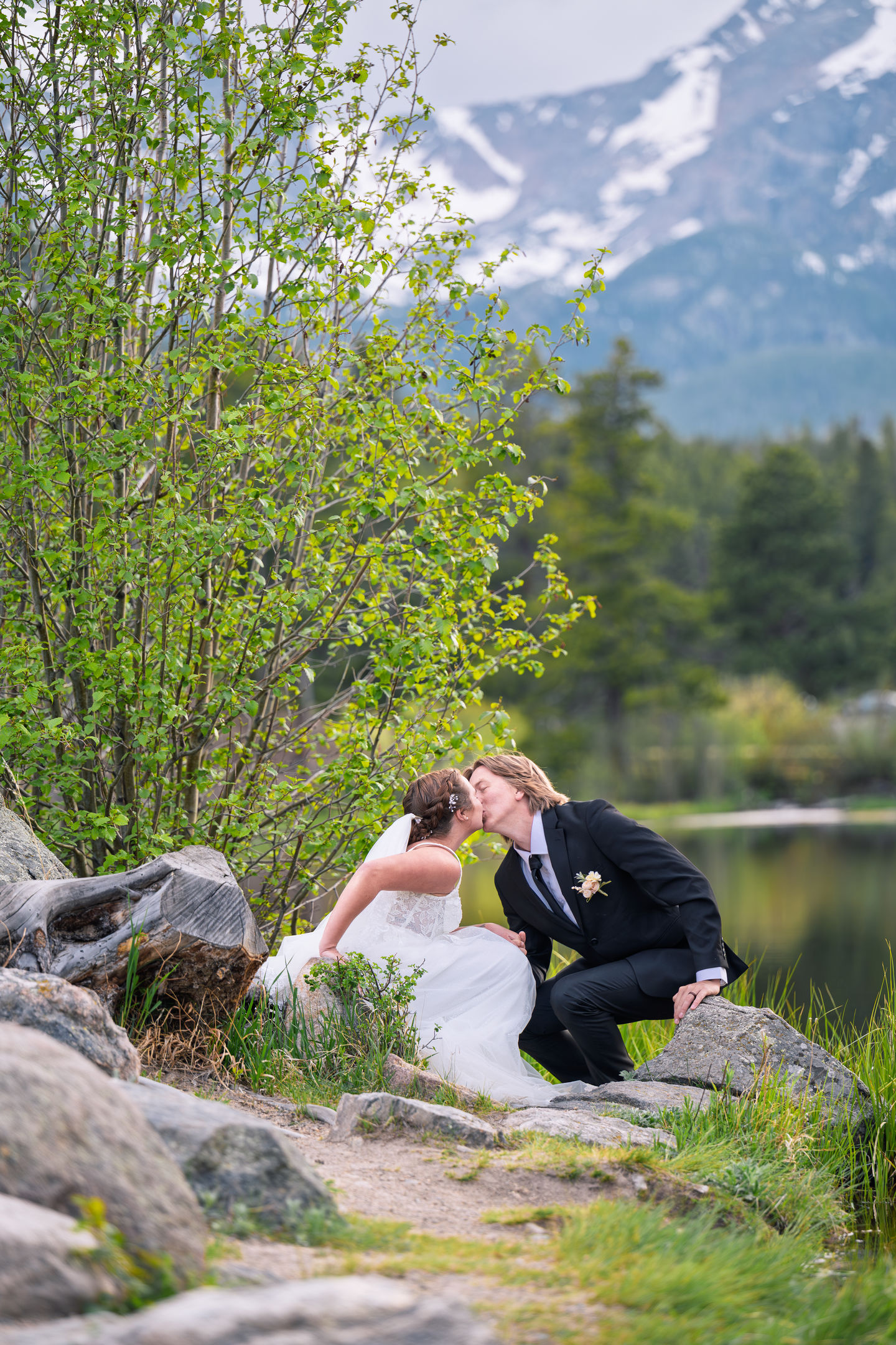 a bride and groom kissing on a rock near a lake
