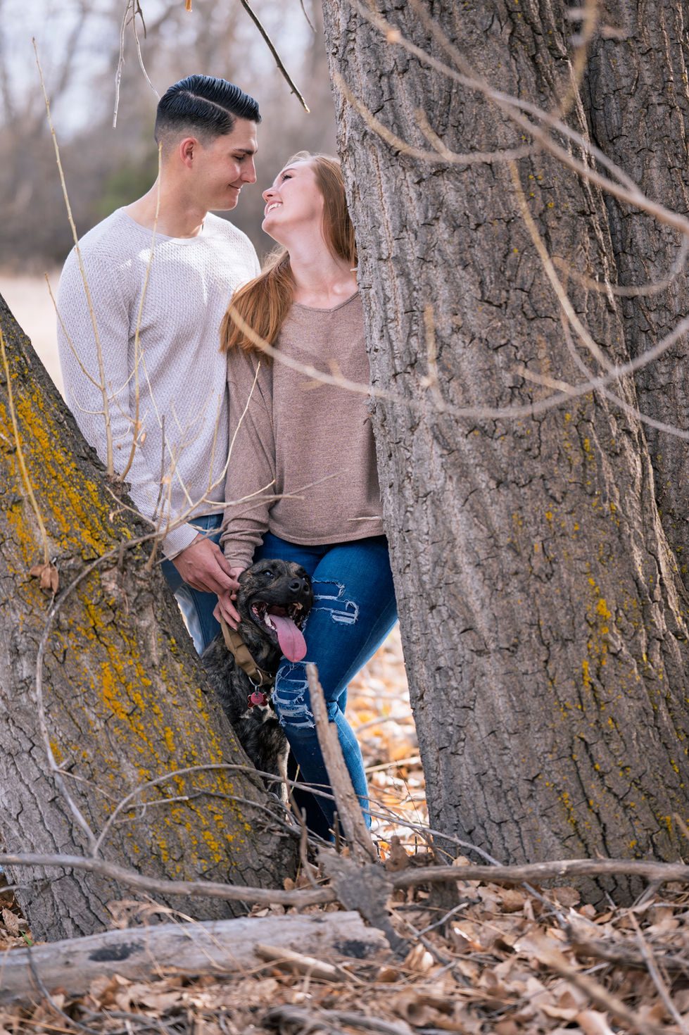 a man and woman standing next to a tree holding a dog