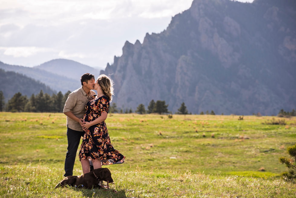 a man and woman kissing in a field with mountains in the background