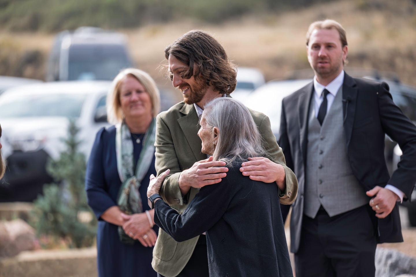 People hugging at an outdoor event, others watching.