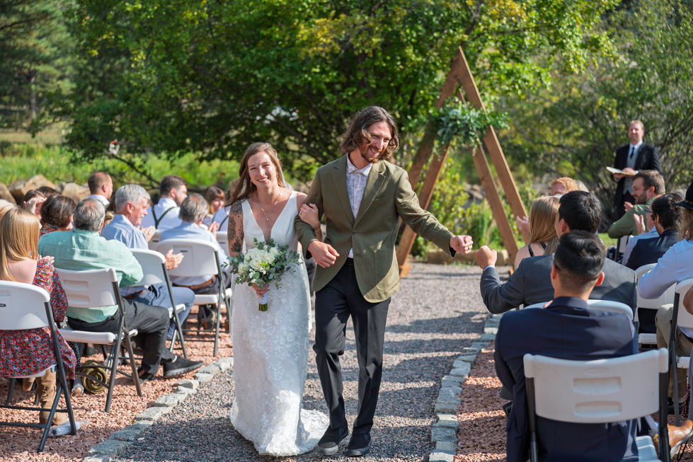 Bride and groom walking down outdoor aisle, smiling.