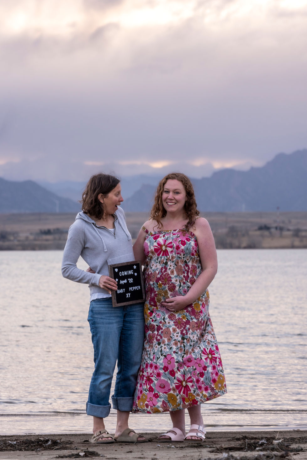 two women holding a sign that says coming april 28 baby pepper