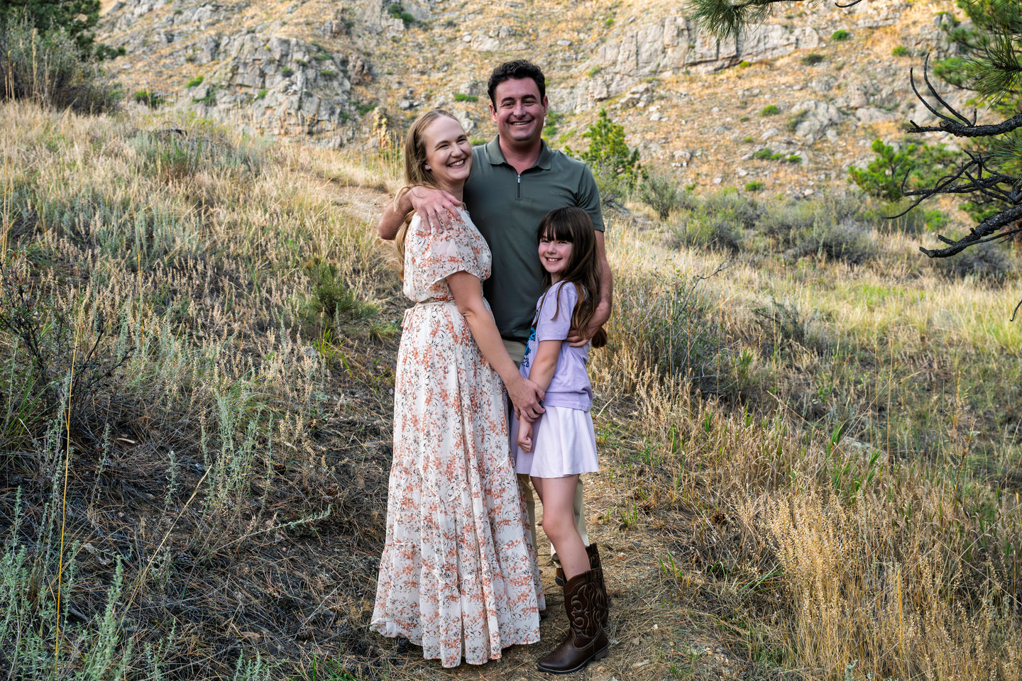 Family posing outdoors on a grassy hillside.