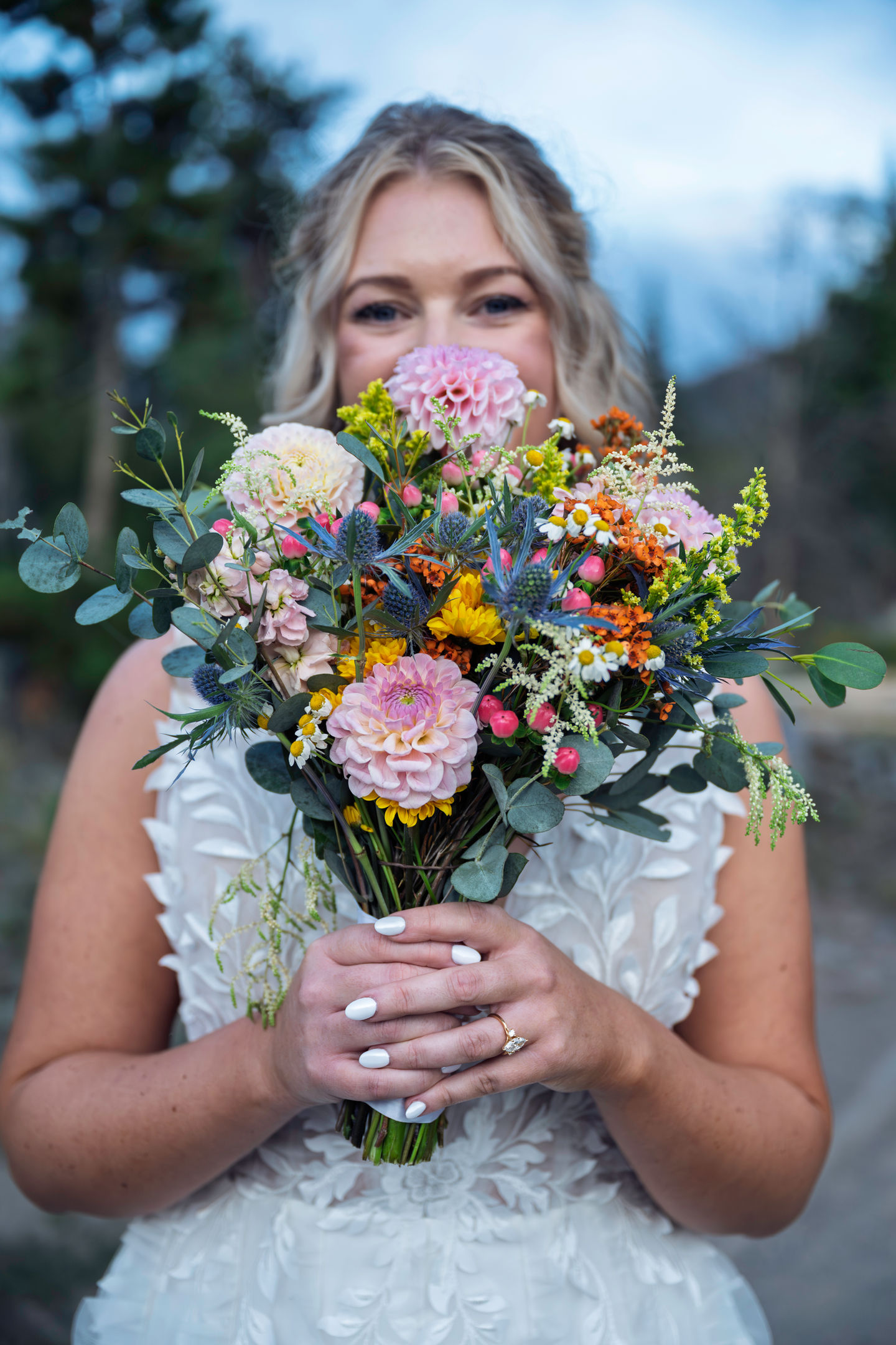 Bride holding colorful flower bouquet outdoors.