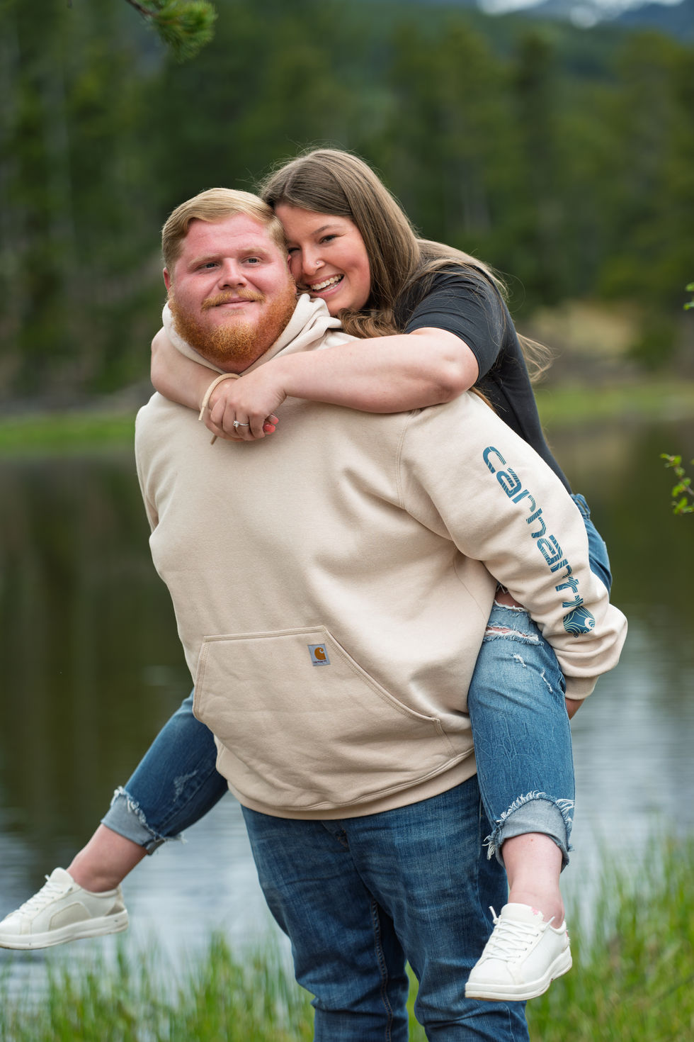 a man wearing a carhartt sweatshirt is carrying a woman on his back
