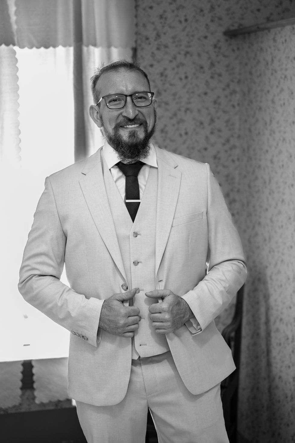 Man in suit smiling, adjusting jacket, black-and-white photo.
