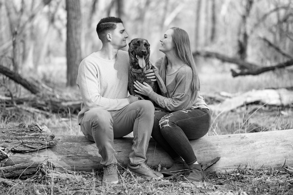 a black and white photo of a man and woman sitting on a log with their dog