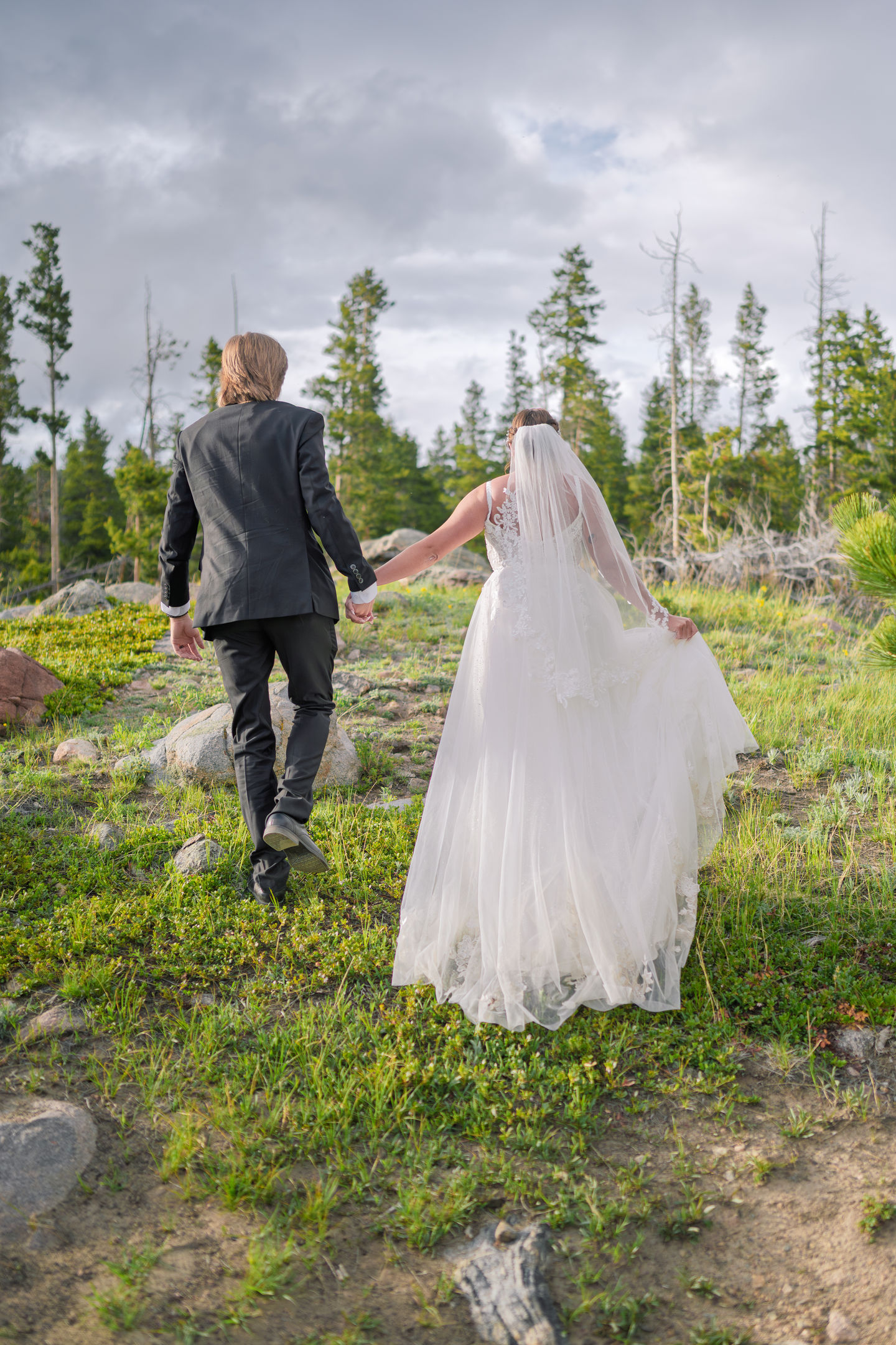 a bride and groom are walking through a field holding hands