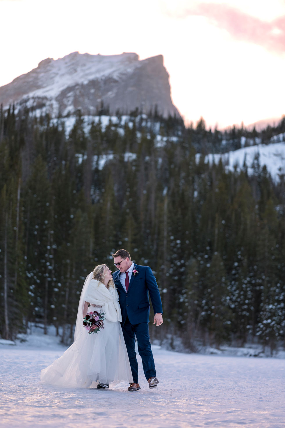 a bride and groom standing in the snow with a mountain in the background