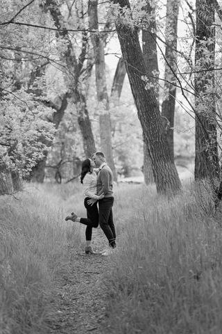 a black and white photo of a man and woman kissing in the woods