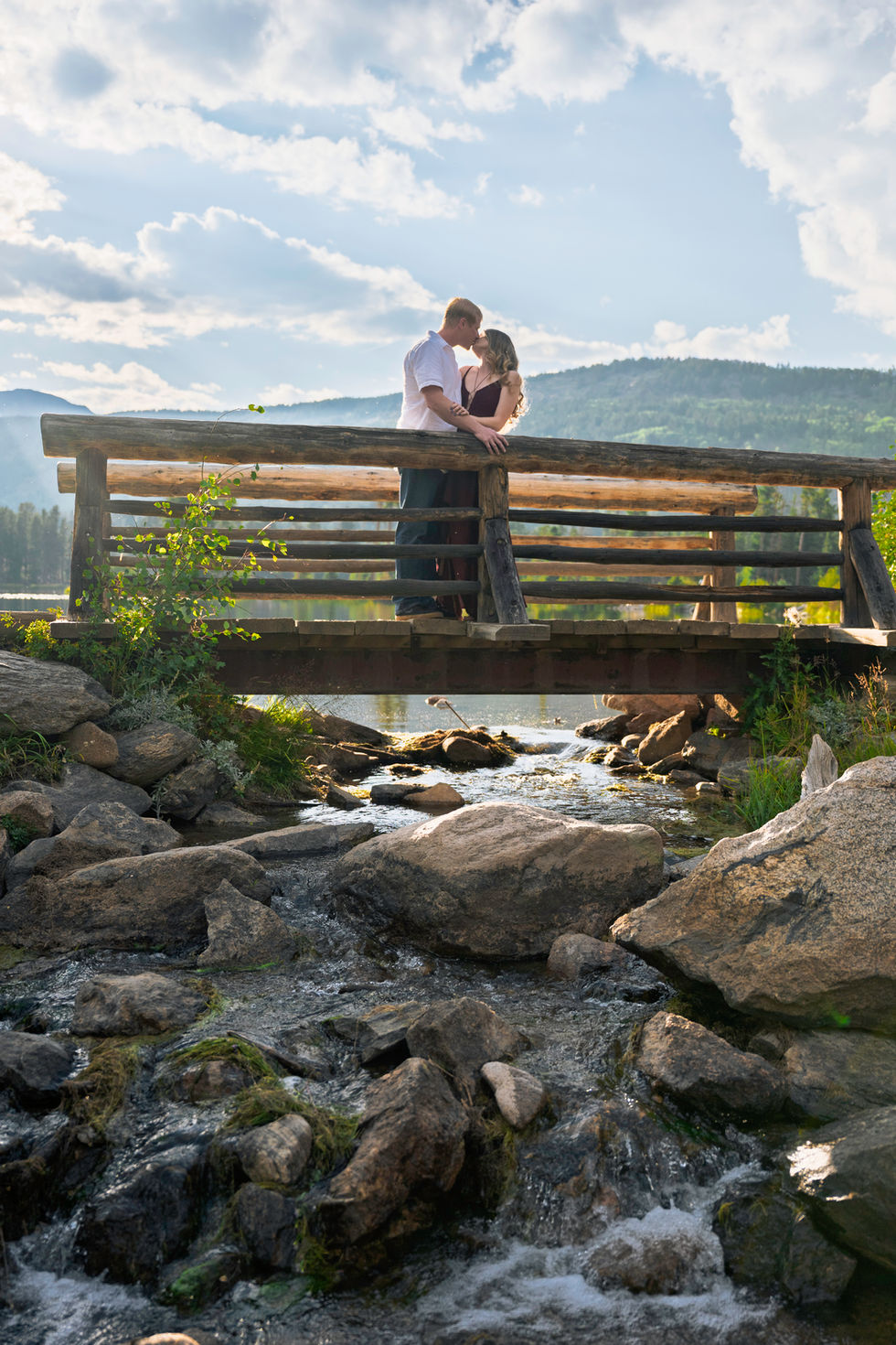 Couple embracing on a wooden bridge over stream.