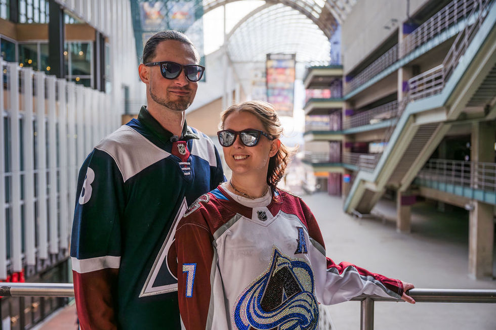Two people wearing hockey jerseys and sunglasses indoors.