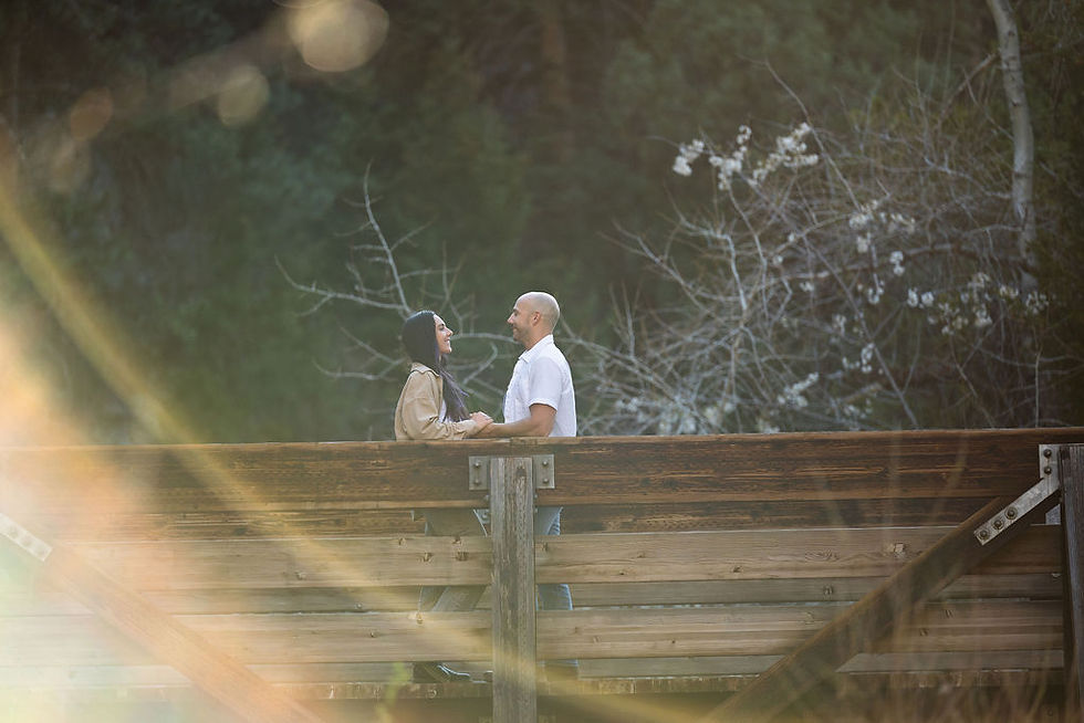 Engaged couple laughing together on a wooden bridge at Eldorado Canyon State Park, warm golden lens flare filtering through cottonwood trees
