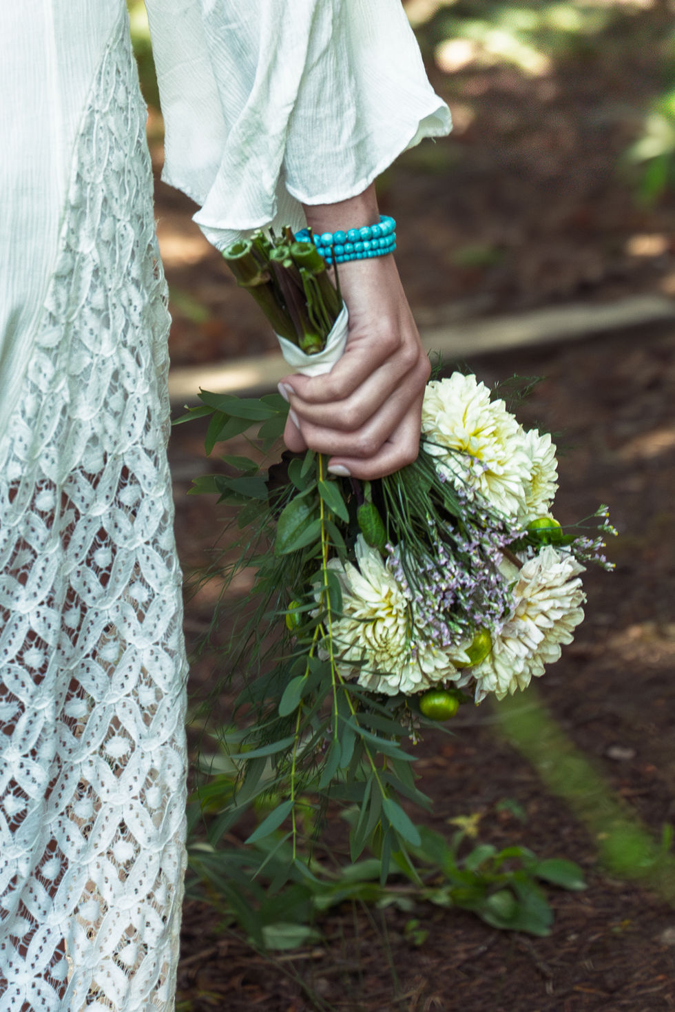 Woman holding bouquet in lace dress outdoors.